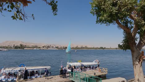 View-of-tourists-on-pier-with-ornamented-tour-boats-on-Nile-river-riverbank,-Luxor