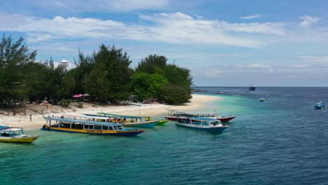tour-boats-anchored-on-white-sand-tropical-beach-at-Gili-Trawangan-Island-on-sunny-summer-day,-aerial