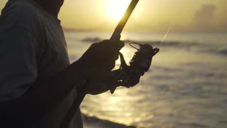 Close-up-on-the-fishing-rod-held-by-an-Indonesian-fisherman-fishing-on-a-coast-of-an-ocean-or-a-sea-at-Sunset-or-sunrise