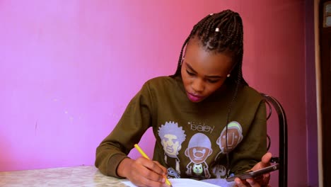 African-woman-writing-on-a-table-holding-a-phone-putting-pen-aside