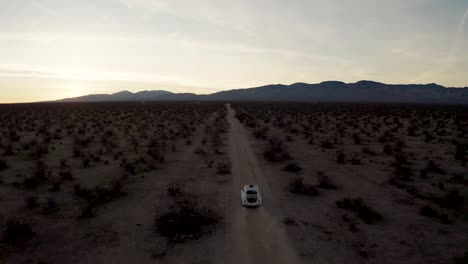 Aerial-drone-shot-flying-behind-white-car-driving-in-Mojave-Desert-wilderness