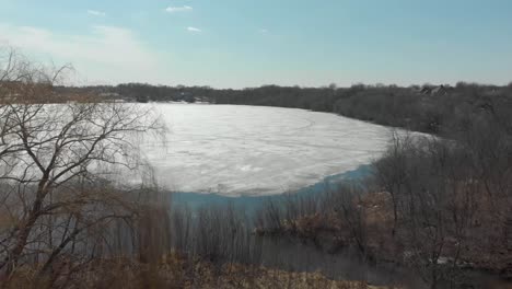 Luftdrohnenvideo-Vom-Lake-Susan-In-Chanhassen,-Minnesota,-Der-Durch-Die-Bäume-Zur-Zurückweichenden-Eisschmelze-Des-Seewassers-Fliegt