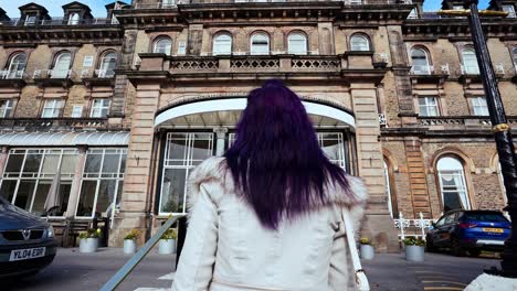 A-young-women-walks-towards-the-huge-luxurious-victorian-Palace-Hotel-in-Buxton,-Derbyshire