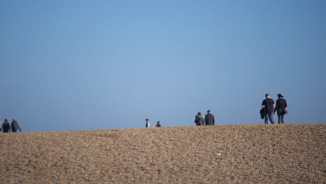 Unrecognizable-tourists-walking-along-the-wooden-walkway-on-Folkestone-shingle-beach,-Kent,-UK