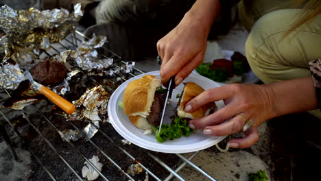 Femail-hands-cutting-burger-in-half-outdoors-by-the-fireplace