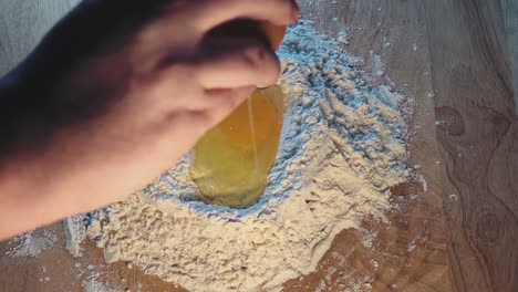 Two-Eggs-Being-Cracked-into-Flour-on-a-Wooden-Work-Surface-for-Baking