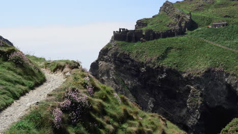 Tourist-on-vacation-walking-on-top-of-a-cliff-along-the-path-that-leads-to-the-ruins-of-Tintagel-castle-in-Cornwall
