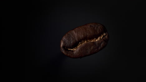 Dunkelbraune-Kaffeebohne-Dreht-Sich-In-Zeitlupe-Vor-Schwarzem-Boden-Mit-Weichem-Licht-Von-Links