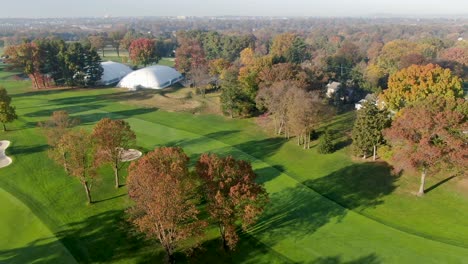 Aerial-turn-in-autumn-reveals-Lancaster-Country-Club-clubhouse,-fairway-and-fall-leaves-in-morning-light