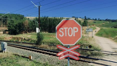 Drone-footage-going-up-and-above-a-stop-sign-by-a-railroad-over-train-lines-with-dirt-road-and-mountains-in-the-background