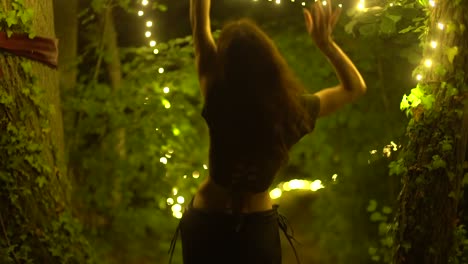 Adorable-Young-Woman-Dancing-On-A-Forest-Nature-Surrounded-By-String-Lights-At-Summer-Evening