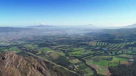 Aerial---Farms-looking-like-stitched-together-patches,-flying-backwards-revealing-edge-of-mountain,-blue-clear-sky