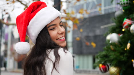 Una-Mujer-Atractiva-Con-Un-Sombrero-De-Santa-En-La-Lista-Traviesa-Frente-A-Un-árbol-De-Navidad-Con-Adornos-Y-Decoraciones-Navideñas