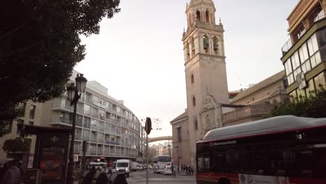 Tilt-Down,-Church-tower-in-Seville,-Spain-with-bus-and-traffic-on-street,-slowmo