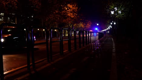 City-street-with-cars-at-night,-abstract-pattern-with-shadow-and-ambulance-flash-lights-moving-close-to-railing-irons-on-sidewalk