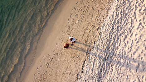 Cute-caucasian-couple-waving-into-drone-camera-on-beach,aerial-top-down
