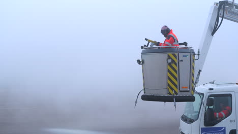 A-man-standing-on-an-aerial-platform-of-a-truck-is-spraying-glycol-fluid-for-aircraft-deicing