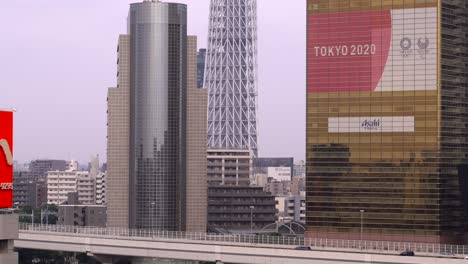 Plakatwerbung-Für-Die-Olympischen-Spiele-2020-In-Tokio-Mit-Autoverkehr-Und-Dem-Sockel-Des-Himmelsbaums-Im-Hintergrund