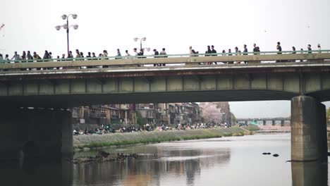 People-Walking-On-The-Bridge-Over-The-Kamogawa-River-In-Kyoto,-Japan,-At-Daytime
