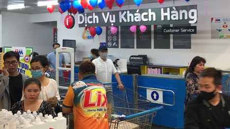 Ein-Supermarktarbeiter-Hat-Im-Vordergrund-Händedesinfektionsmittel-Vorrätig,-Während-Im-Hintergrund-Vietnamesische-Käufer-Mit-Gesichtsmasken-In-Ho-Chi-Minh-Stadt,-Vietnam,-Am-7.-März-2020-Vorbeigehen
