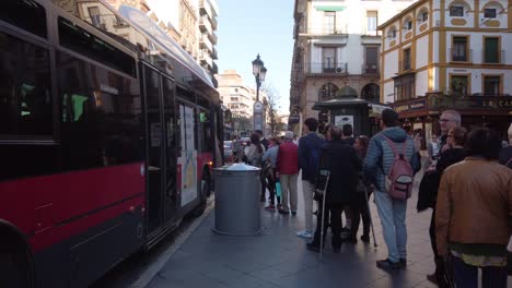 Long-line-of-people-wait-patiently-to-board-bus-at-bus-stop-in-Seville