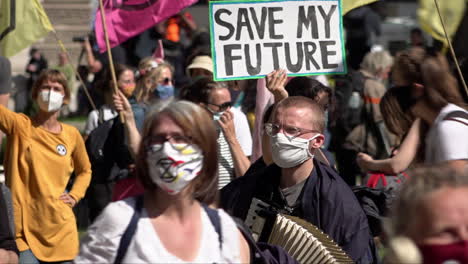 Extinction-Rebellion-climate-change-protestors-wearing-protective-face-masks-due-to-the-Coronavirus-pandemic-dance-in-front-of-someone-holding-up-a-placard-that-says,-“Save-my-future”