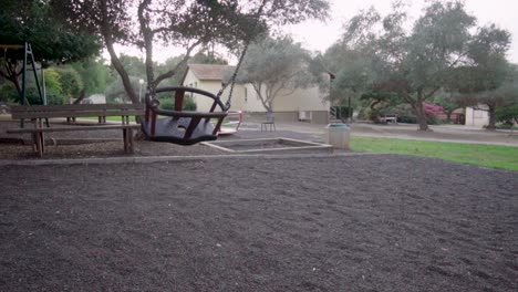 swing-moves-in-slow-motion-at-a-playground,-trees-in-the-background,-day