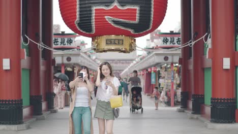 Two-Young-Japanese-Girls-Taking-Selfies-At-The-Kaminarimon-Gate-Senso-Ji-In-Asakusa,-Tokyo,-Japan