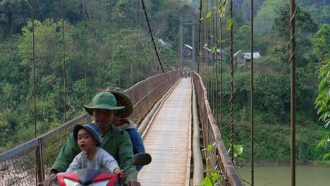 Asiatische-Familie-Mit-Kind-Auf-Dem-Moped,-Das-Holz-Und-Hängebrücke-über-Den-Fluss-überquert,-Vietnam