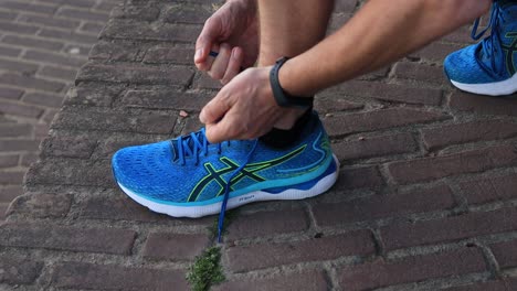 Squatted-athlete-trail-runner-hands-with-pedometer-on-wrist-tie-shoe-laces-securely-in-a-tight-knot-before-a-run-on-sidewalk