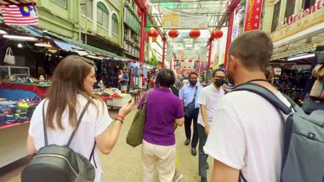 Following-shot-of-foreign-tourists-enjoying-a-walk-through-crowded-roadside-stalls-in-street-market-in-Kuala-Lumpur,-Malaysia-at-daytime