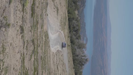 Un-Auto-Circulando-Por-Una-Carretera-En-Las-Colinas-De-Patagonia,-Argentina-Con-Montañas-Y-Un-Lago-Al-Fondo