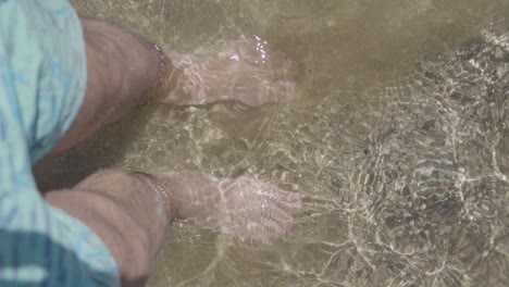 Bird's-eye-view-of-a-man's-feet-in-clear-water-on-the-beach