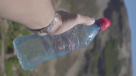 Ein-Mann-Im-Urlaub-Hält-Eine-Wasserflasche-In-Der-Hand-Und-Zeigt-In-Zeitlupe-Einen-Panoramablick-Auf-Hügel,-Wälder-Und-Einen-See-In-Patagonien,-Argentinien