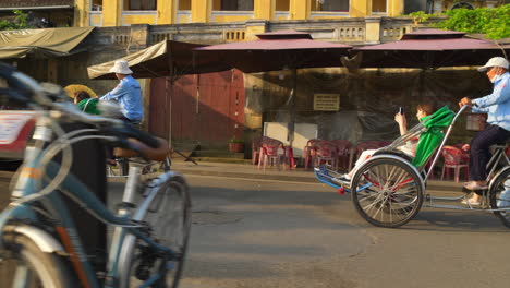 Una-Filmación-Dinámica-De-Turistas-Que-Viajan-En-Un-Ciclo-De-Transporte-De-Alquiler-Para-Recorrer-La-Ciudad-De-Hoi-An-En-Vietnam
