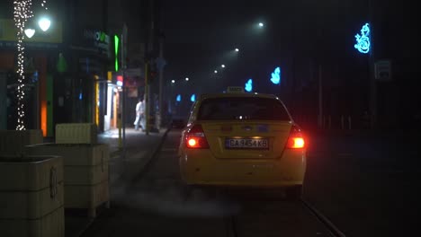 Taxi-cab-idles-outside-of-empty-restaurant-and-shops-at-night-time