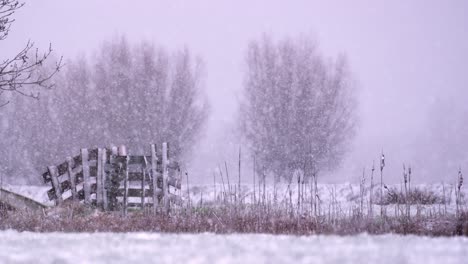 Beautiful-static-show-of-heavy-snow-fall-on-part-of-an-old-wooden-fence-in-the-middle-of-a-field,-slow-motion