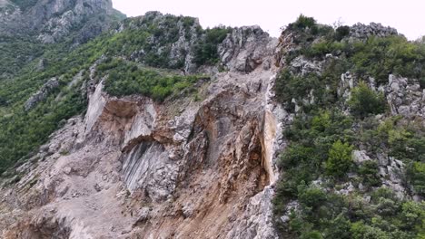 Aerial-shot-of-erosion-on-hillside-with-rocky-terrain-and-forest-near-mountain