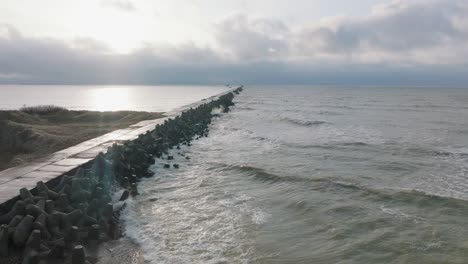 Aerial-establishing-view-of-Port-of-Liepaja-concrete-pier,-Baltic-sea-coastline-day,-big-waves-splashing,-slow-motion-birdseye-drone-shot-moving-forward