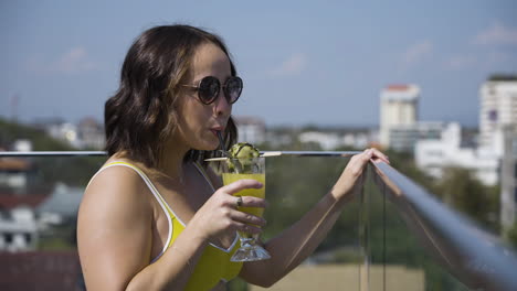Slow-motion-shot-of-a-female-in-a-bright-bikini-drinking-her-cocktail-on-a-balcony