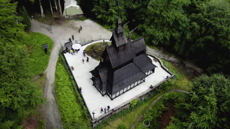 Drone-shot-rising-away-from-a-Stave-church-in-cloudy-Fantoft,-Norway