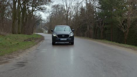 Front-view-of-a-Suv-Mazda-car-driving-through-empty-forest-road-on-a-rainy-day