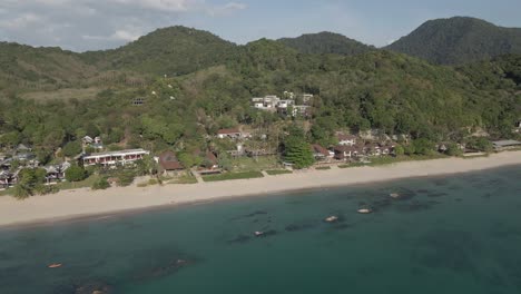 Aerial-retreats-from-quiet-Koh-Lanta-beach-resorts,-island-mountains