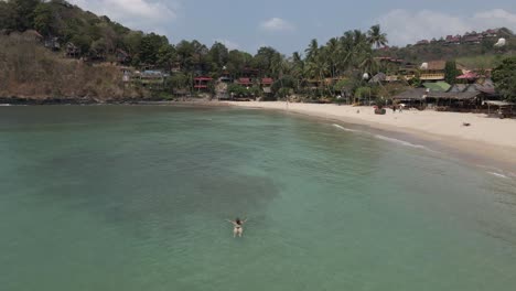 Woman-in-bikini-swims-in-shallow-water-off-sandy-beach-on-Koh-Lanta