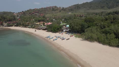 Aerial-pulls-back-from-blue-fishing-boats-on-Kantiang-Bay-sand-beach