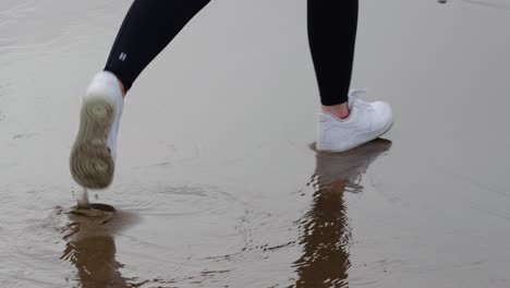 Girl-in-white-sports-trainers-running-through-wet-soggy-sand-to-avoid-getting-wet-as-footprints-disappear-instantly