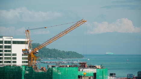 Construction-Site-with-Building-Crane-on-Top-of-New-Skyscraper,-Kota-Kinabalu-City-Water-Villages-by-Gaya-Island-in-Background