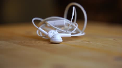 White-in-ear-headphones-with-cable-and-aux-plug-lies-on-a-light-wooden-board-and-rotates