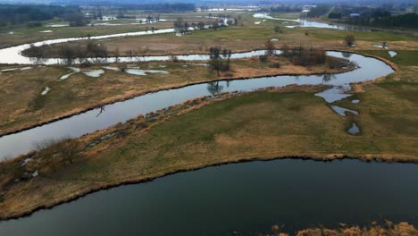 Luftaufnahmen-Von-überschwemmten-Feldern-Auf-Dem-Land,-Mit-Einem-Sich-Schlängelnden-Fluss-Und-Sonnenreflexionen-Auf-Dem-Wasser