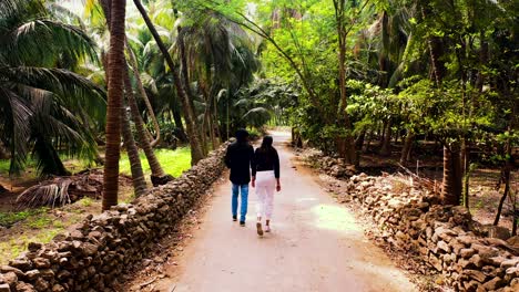 beautiful-couple-walking-off-the-road-on-both-sides-of-palm-trees,-vacation-concepts-of-the-couple,-beautiful-palm-forest-area,-and-camera-following-the-couple